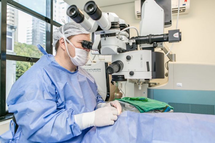 médico caucasiano em sala de cirurgia, usando luvas e operando os olhos de um paciente, utilizando um aparelho de última tecnologia