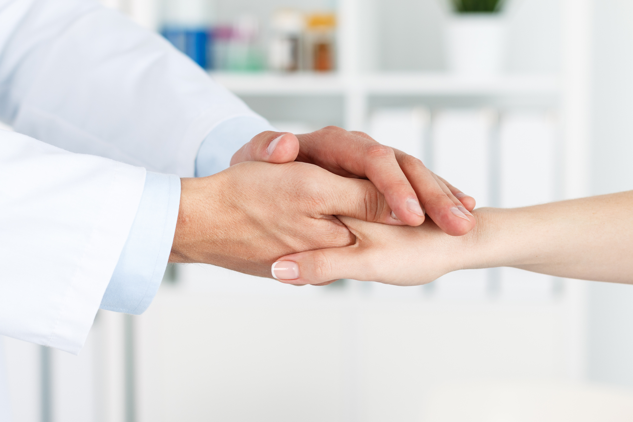 Friendly male doctor's hands holding female patient's hand for encouragement and empathy. Partnership, trust and medical ethics concept. Bad news lessening and support. Patient cheering and support