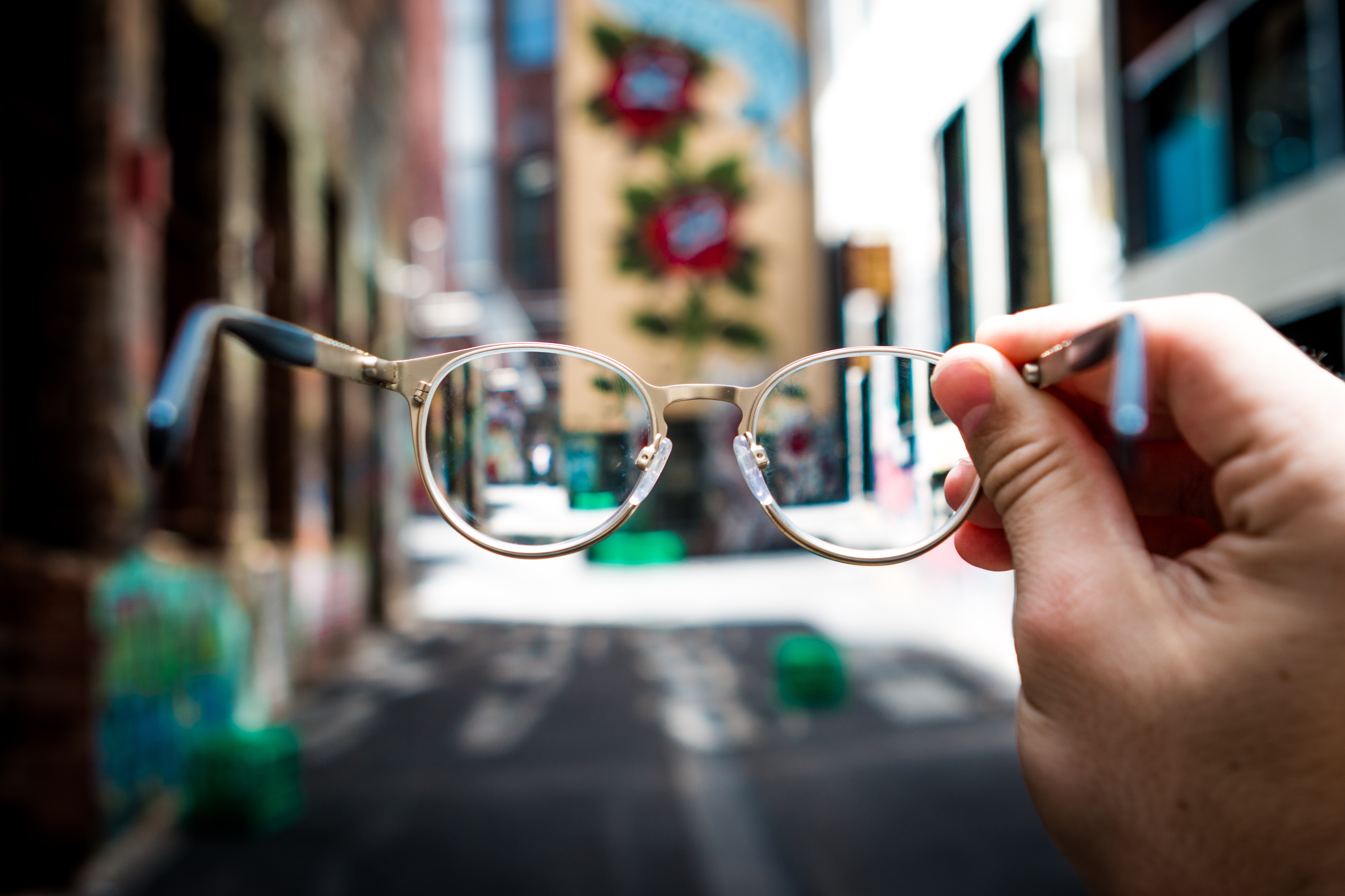 erro de refração mão segurando óculos de grau na frente de um prédio grafitado. fora do óculos está tudo embaçado, pelas lentes a imagem está nítida.