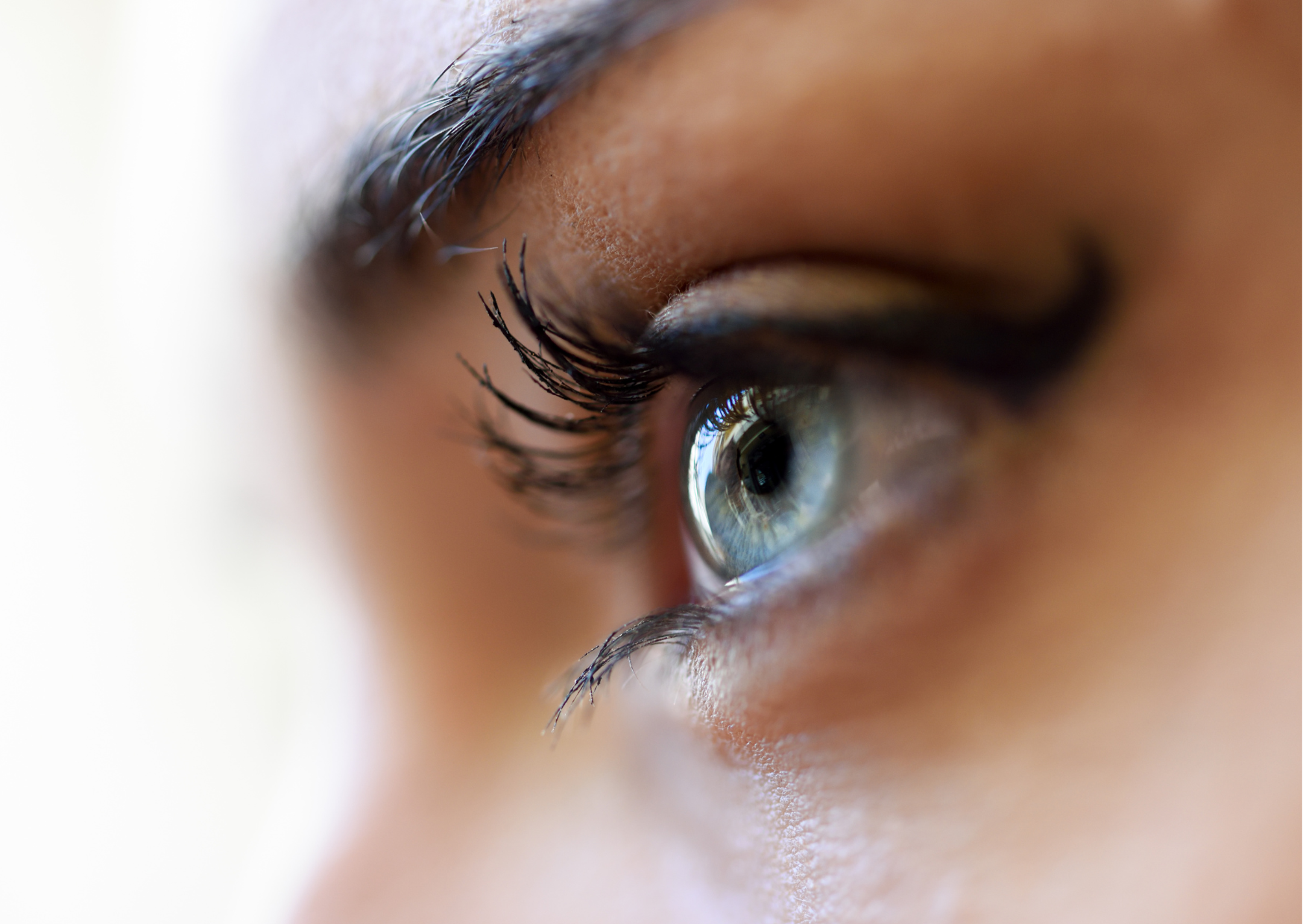 fundo branco; ao lado direito, em zoom, rosto humano, de uma mulher, em perfil, destacando a área do olho, que está aberto e é da cor verde; exemplificando o que é ceratocone e como ela afeta a visão.