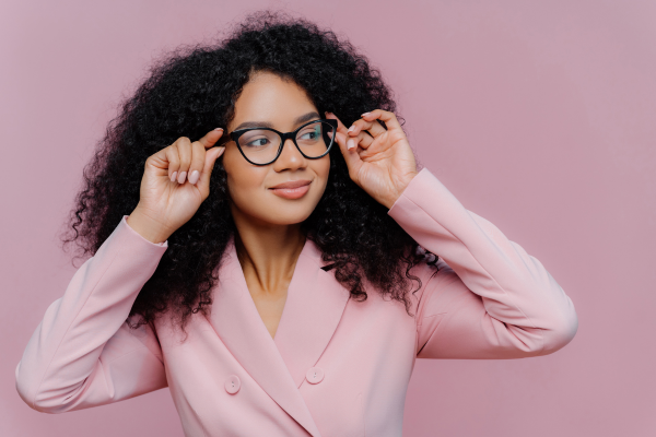 mulher negra sorridente com óculos de grau em fundo rosa ilustra artigo sobre mitos e verdades ao usar óculos de outra pessoa