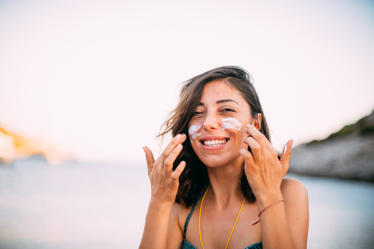mulher parda jovem e sorridente tem duas marcas de protetor solar no rosto para ilustrar artigo sobre a relação entre o produto e a alergia nos olhos