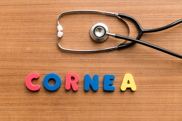 letras coloridas formando a palavra CORNEA e um estetoscópio em cima da mesa ilustram artigo sobre uso de óculos e doação de córnea.