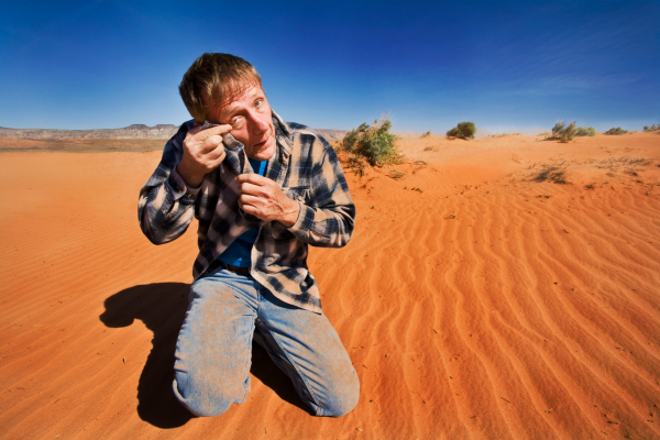 homem coça o olho no deserto para ilustrar artigo sobre sensação de areia nos olhos