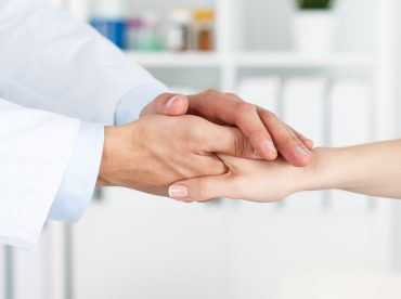 Friendly male doctor's hands holding female patient's hand for encouragement and empathy. Partnership, trust and medical ethics concept. Bad news lessening and support. Patient cheering and support