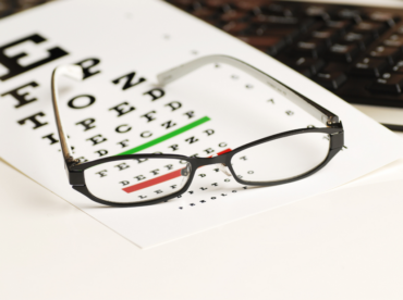 óculos de grau em cima de folha de exame de vista com letras maiores e miúdas ilustra artigo sobre os perigos do exame grátis, muito realizado em óticas