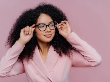 mulher negra sorridente com óculos de grau em fundo rosa ilustra artigo sobre mitos e verdades ao usar óculos de outra pessoa