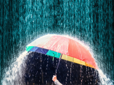 mão humana segura guarda-chuva colorido sob forte tempestade para ilustrar artigo sobre a relação entre período de chuvas e doenças oculares