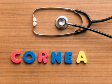 letras coloridas formando a palavra CORNEA e um estetoscópio em cima da mesa ilustram artigo sobre uso de óculos e doação de córnea.