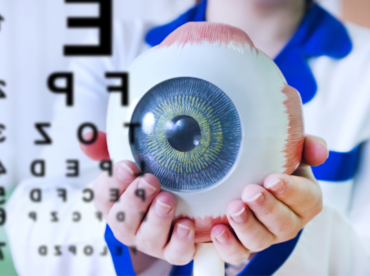 mulher de jaleco segura prótese ocular grande, de amostra, para ilustrar artigo sobre glaucoma secundário