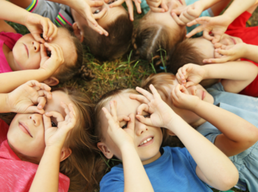 crianças caucasianas com as mãos sobre os olhos ilustram artigo sobre melhores óculos para crianças em idade escolar